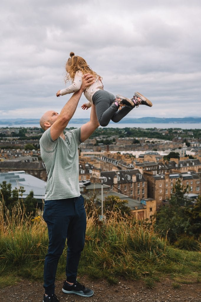 Parent lifting child into the air overlooking Edinburgh