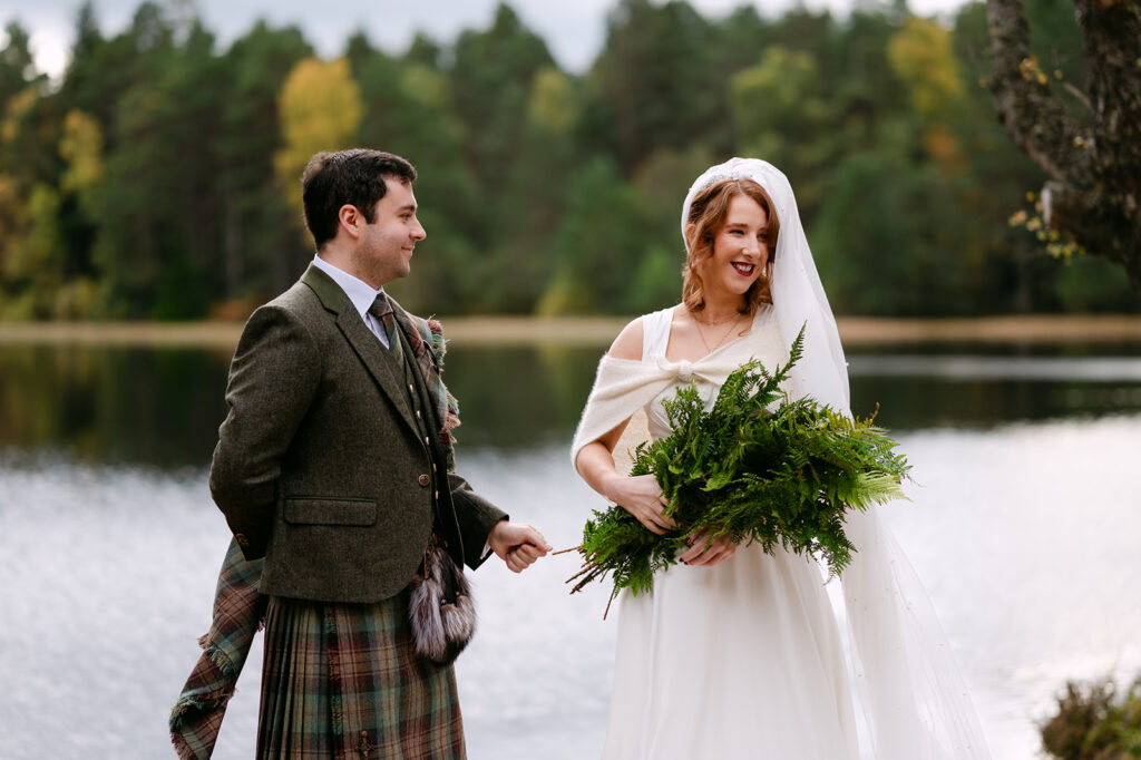 Couple smiling during outdoor wedding ceremony by water.