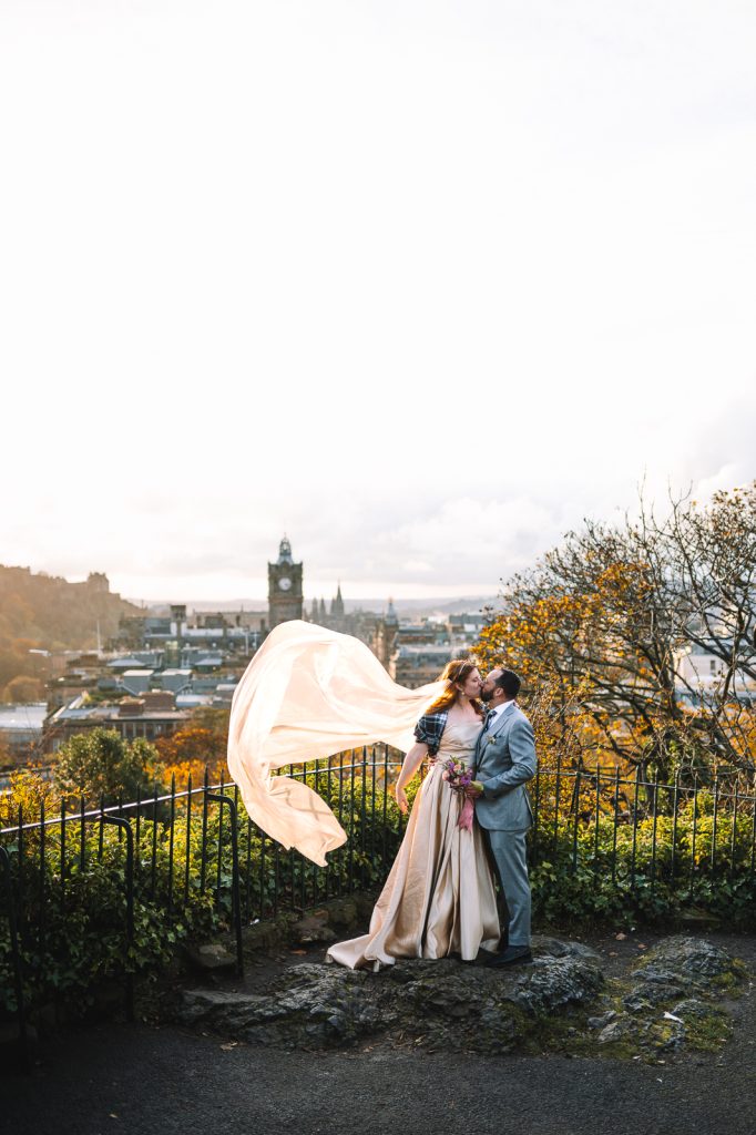 Bride and groom with veil flowing in windy hillside