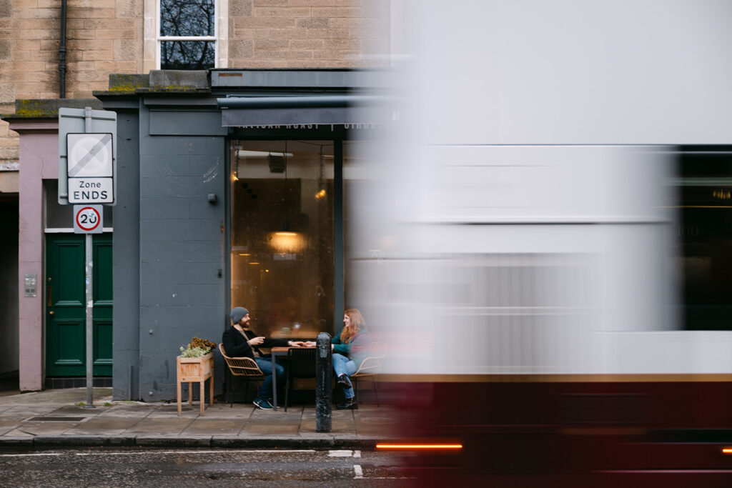 couple sits outside a coffee shop in Stockbridge as a bus goes by