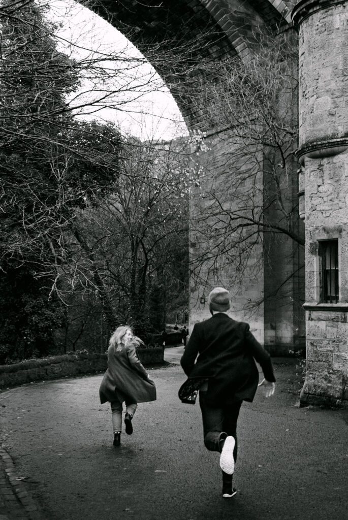 woman runs playfully away from man at the water of Leith