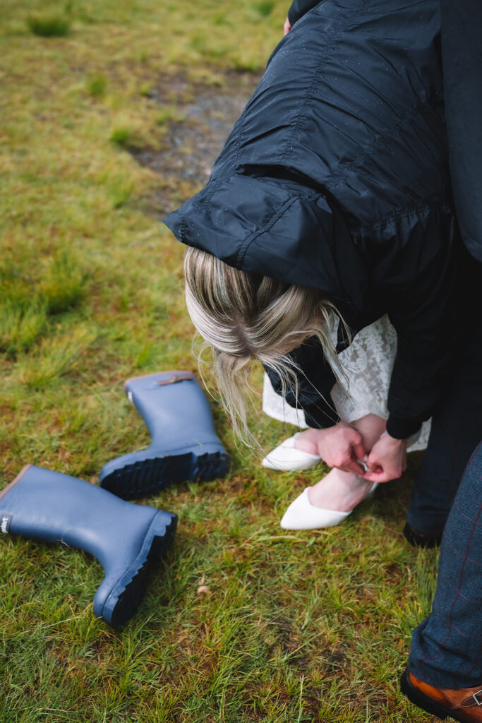Bride adjusting shoes outdoors before ceremony in natural setting.