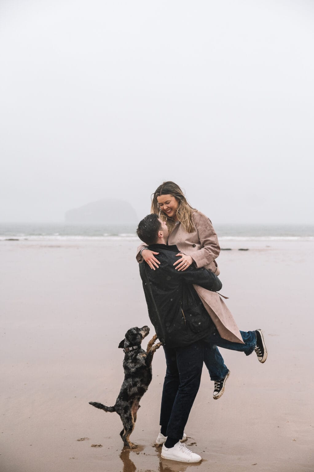 Couple embracing on rocky beach with dog