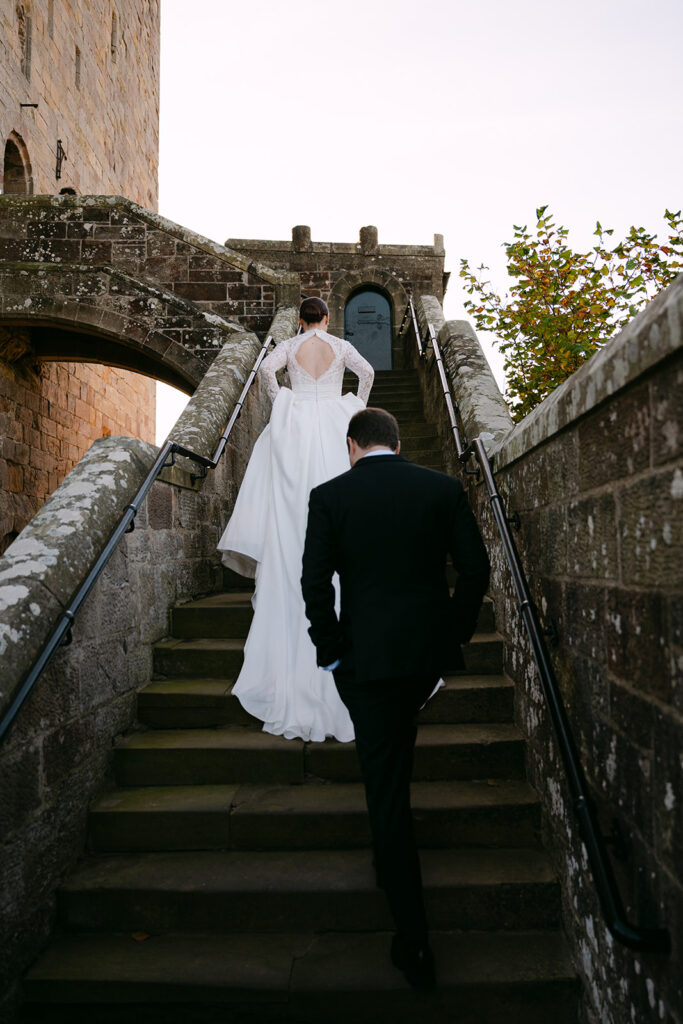Bride and groom walking up stone staircase toward historic building.