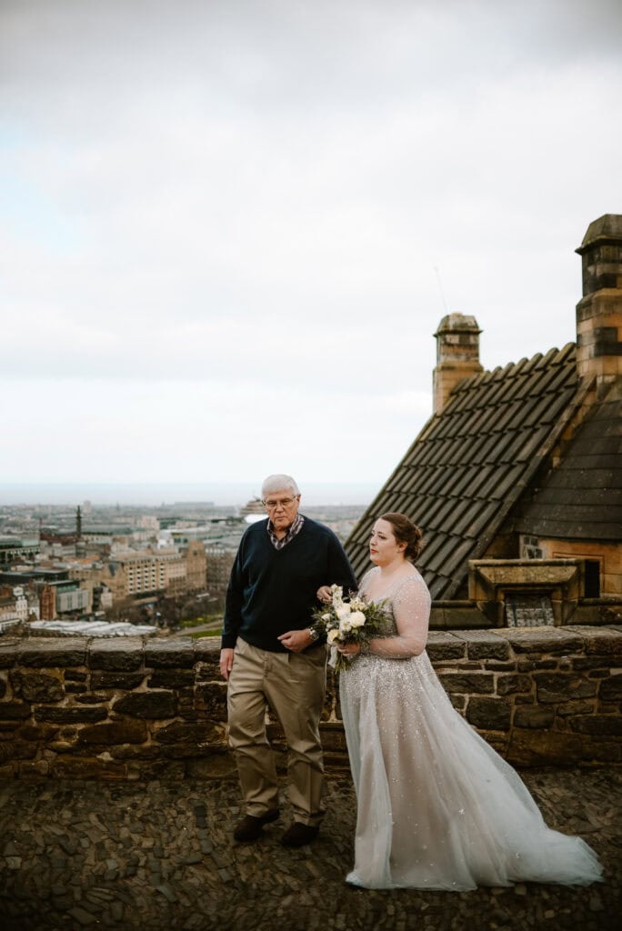 bride and father standing together overlooking Edinburgh cityscape