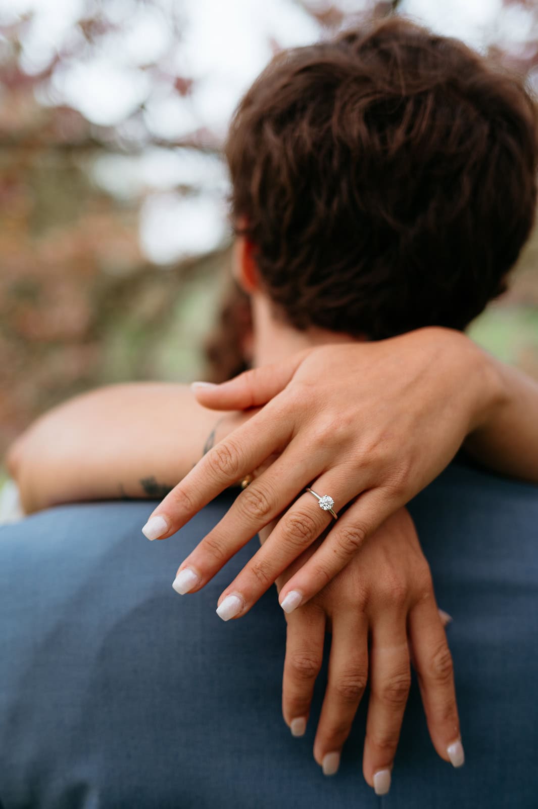 Close-up of bride’s hand with engagement ring resting on partner’s shoulder