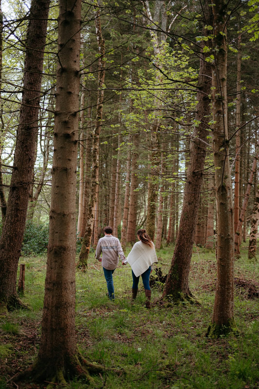 Couple walking through forest pathway surrounded by tall trees