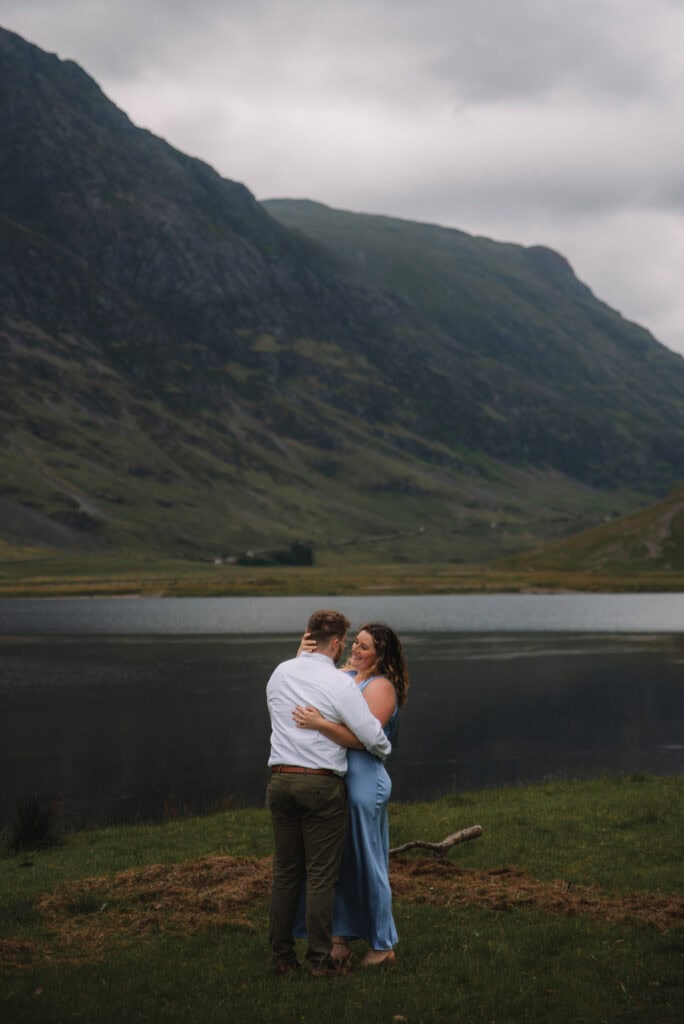 Couple embracing beside a calm Highland lake with mountains behind