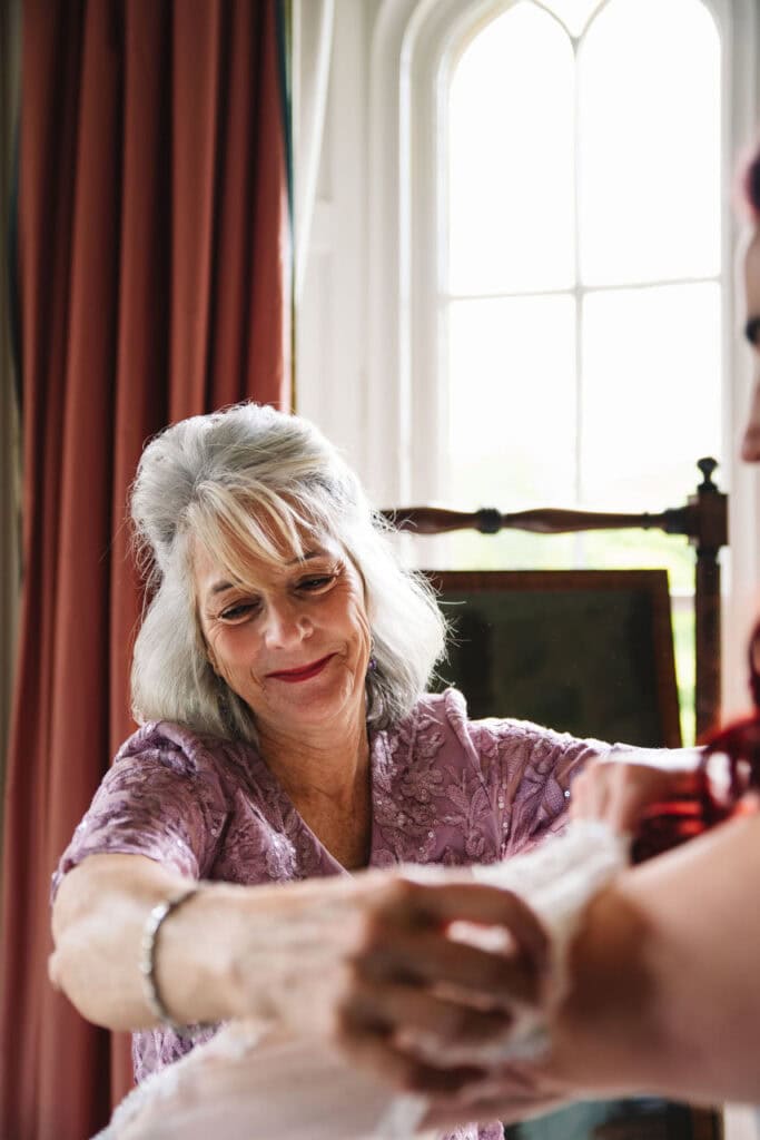 Mother helping bride get ready in a softly lit room before the wedding