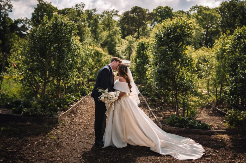 Bride and groom embracing in a garden pathway lined with greenery