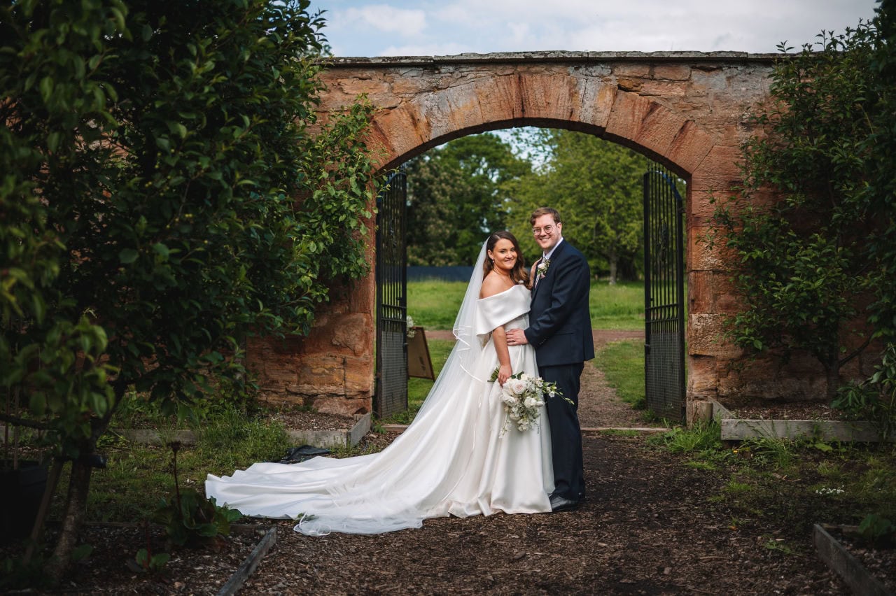 Couple posing beneath a stone archway in a garden venue