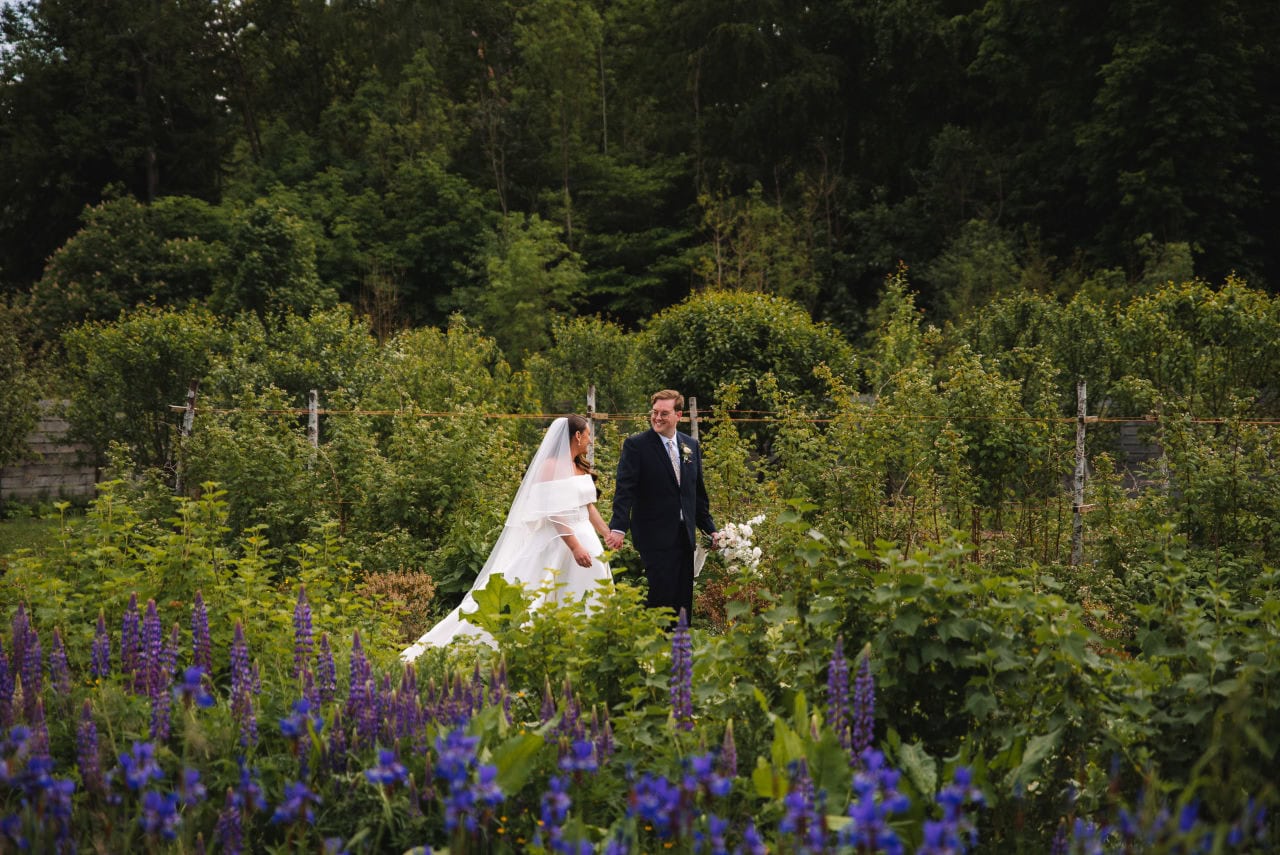 Bride and groom walking together through a garden with wildflowers