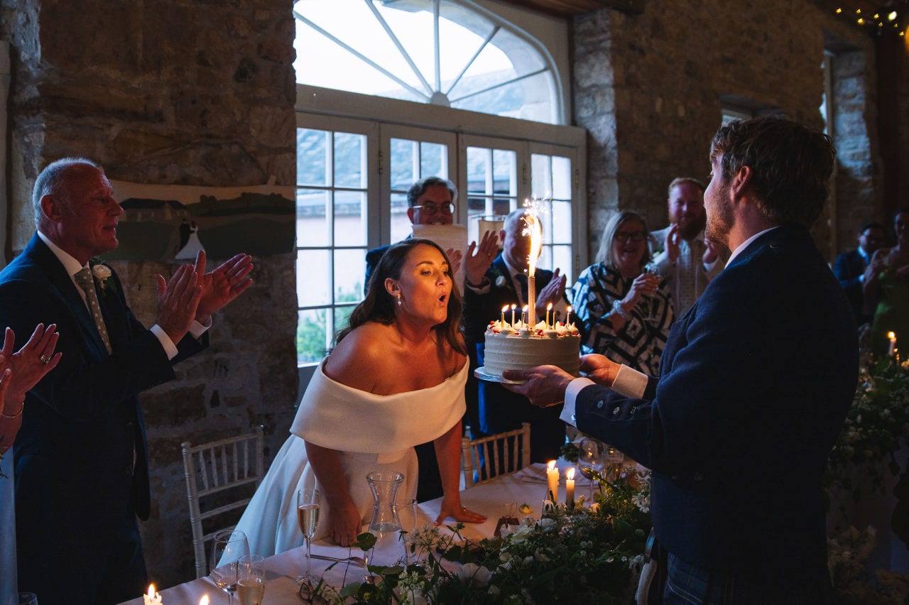 Bride blowing out candles on wedding cake during reception
