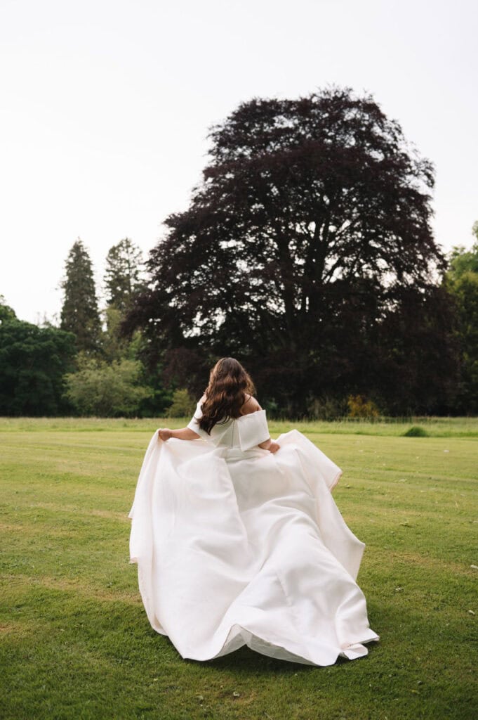 Bride walking across a wide green lawn holding her dress