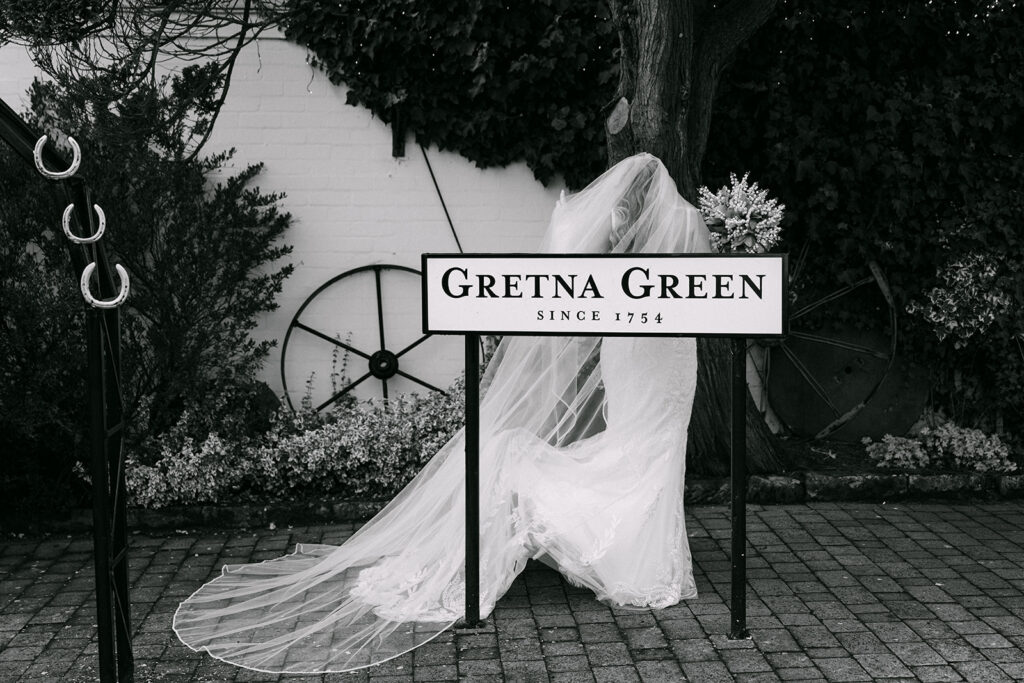 bride stands behind the gretna green sign