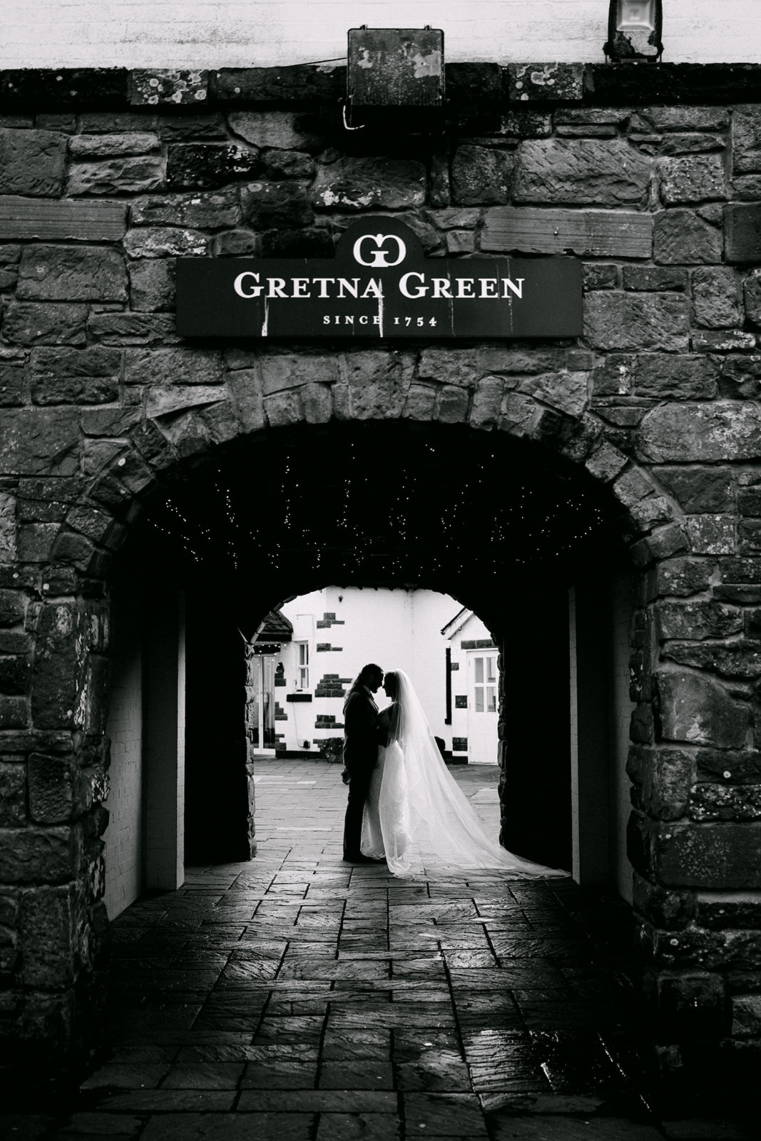 bride and groom stand silhouetted archway with gretna green sign