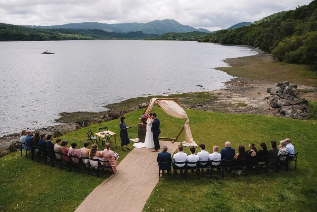 Guests seated at outdoor ceremony beside loch