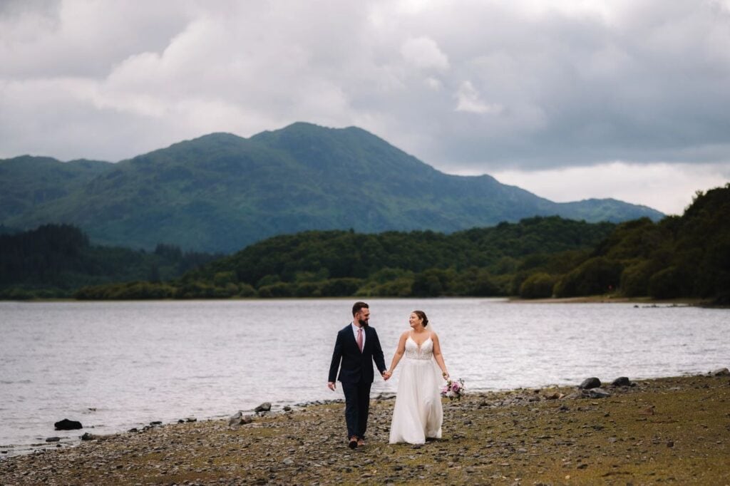 Couple walking beside loch with mountains behind