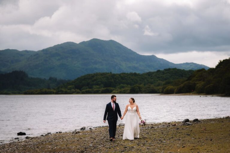 Couple walking beside loch with mountains behind