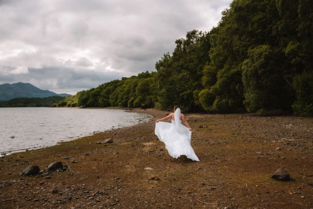 Bride walking alone along lakeside shore