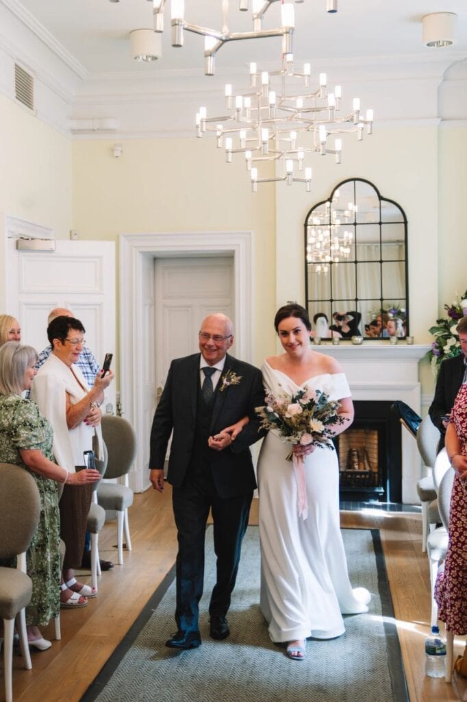 Bride walking down aisle with family member in elegant room