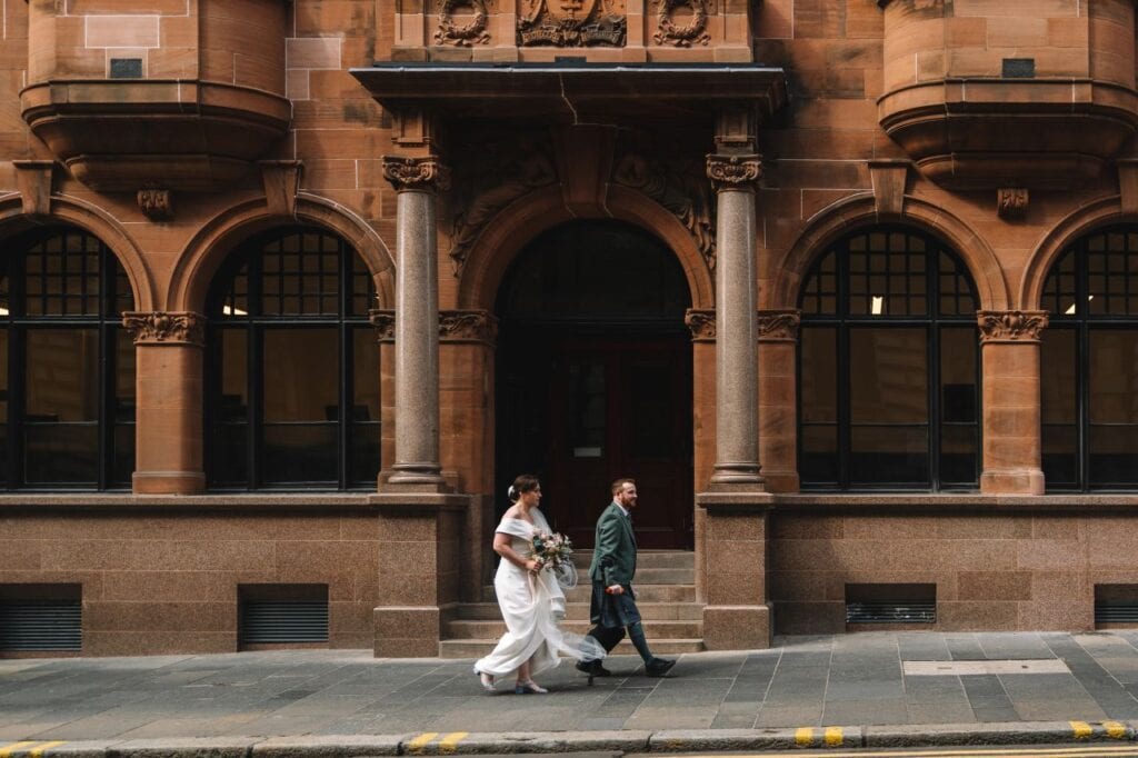 Bride and groom walking past historic Edinburgh building