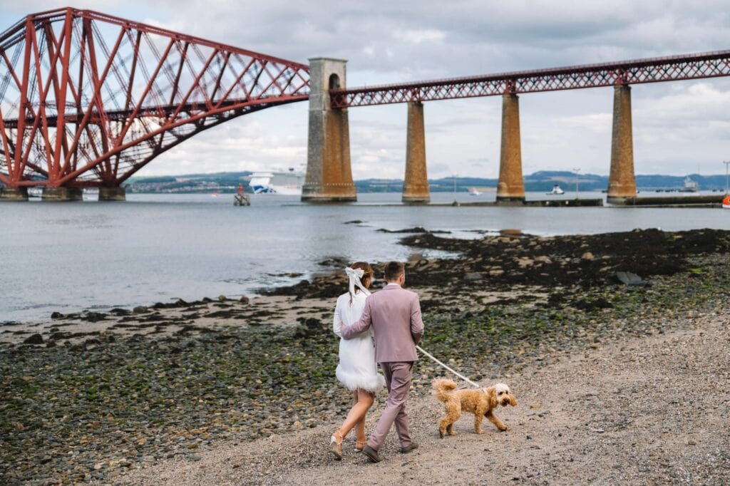 Couple walking dog along rocky shoreline in Scotland