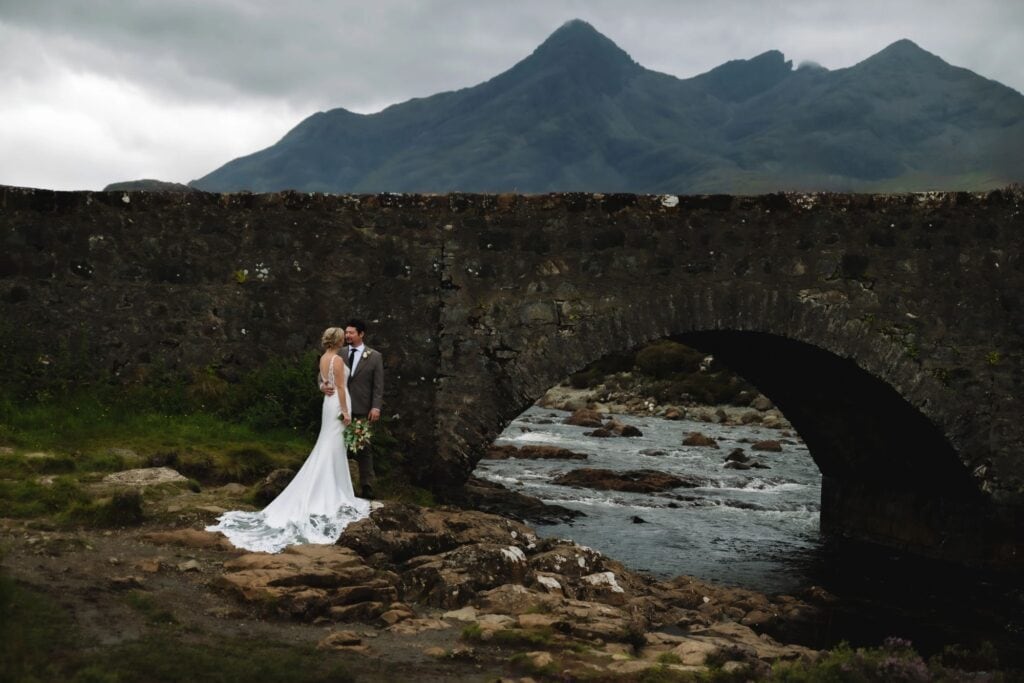 Couple standing by river under stone bridge in Scotland