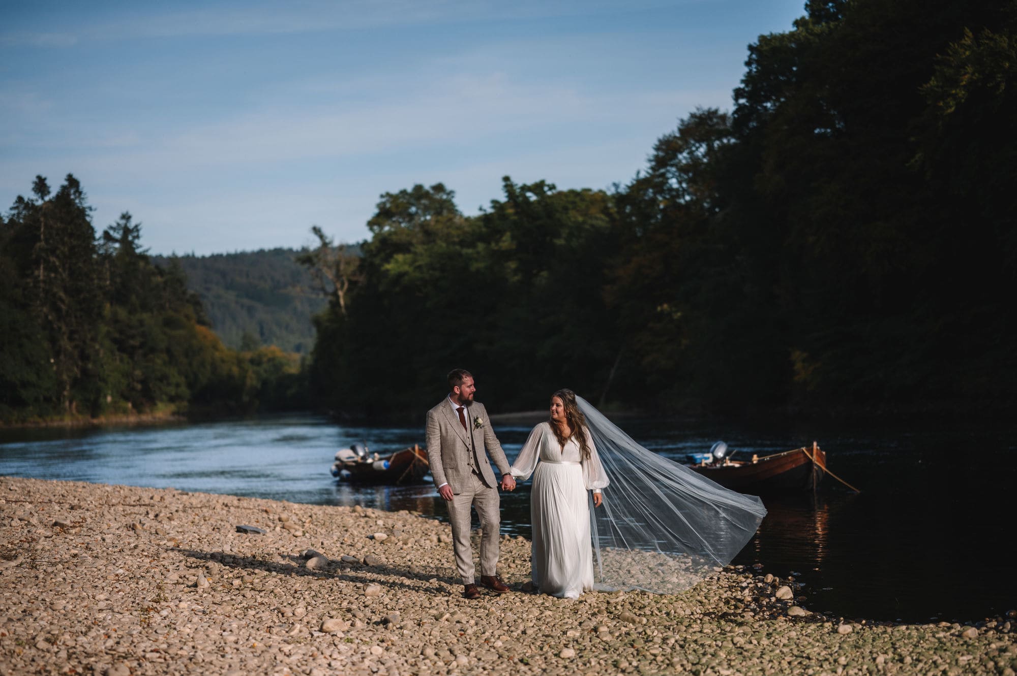 Couple walking along riverbank with flowing veil
