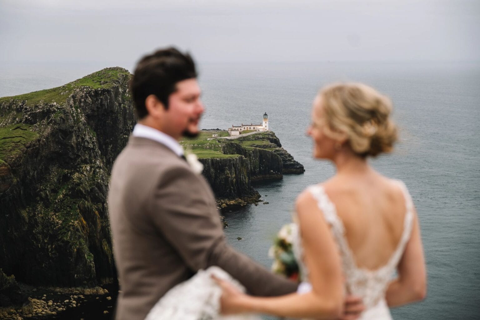 Couple holding hands on cliff overlooking Scottish coastline