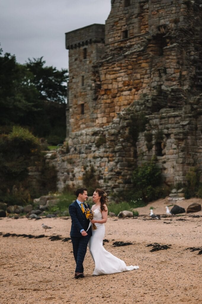  Couple standing on beach with castle ruins behind