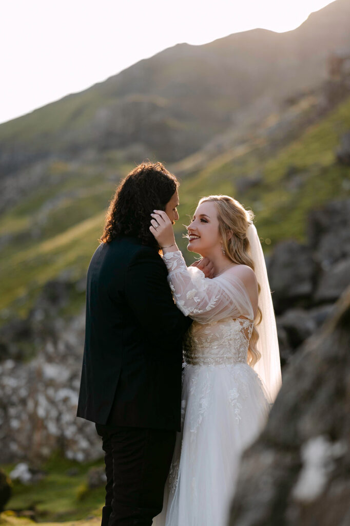 Couple sharing intimate moment on hillside with mountain backdrop.