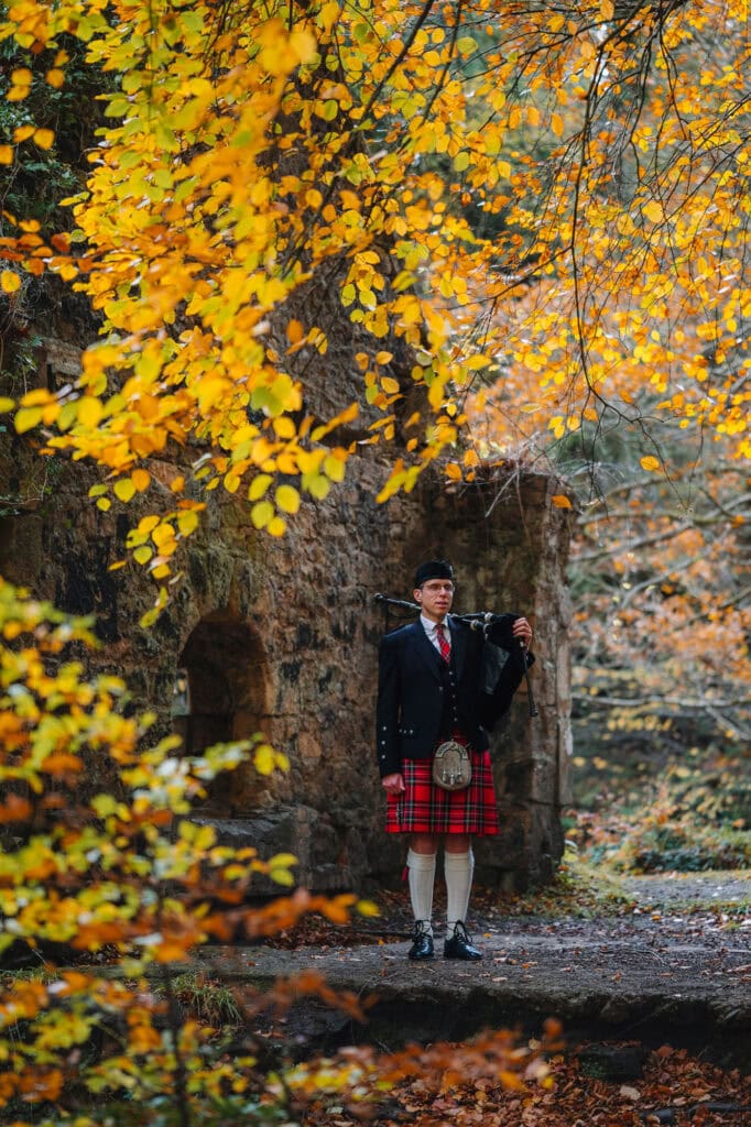 bagpiper standing alone in woodland wearing traditional kilt