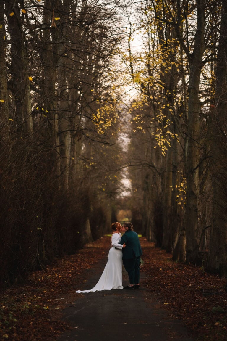 Couple walking through woodland path during autumn wedding