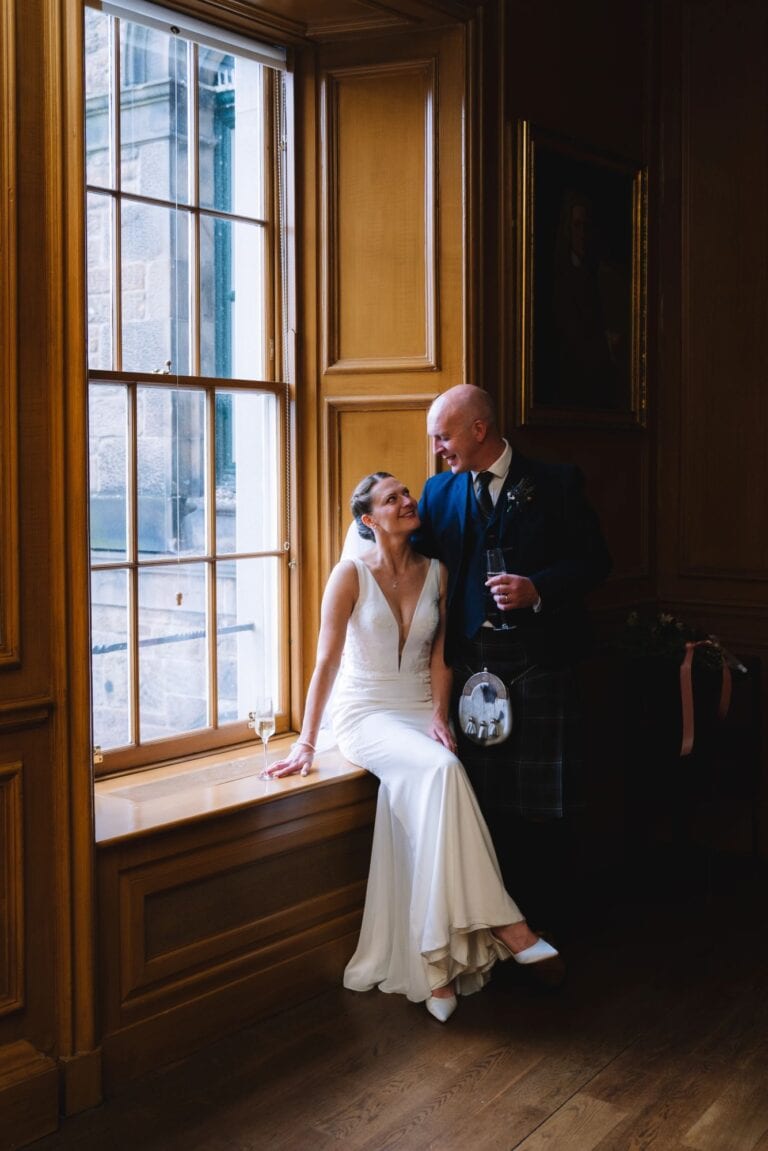 Bride and groom by window in warm indoor wedding portrait