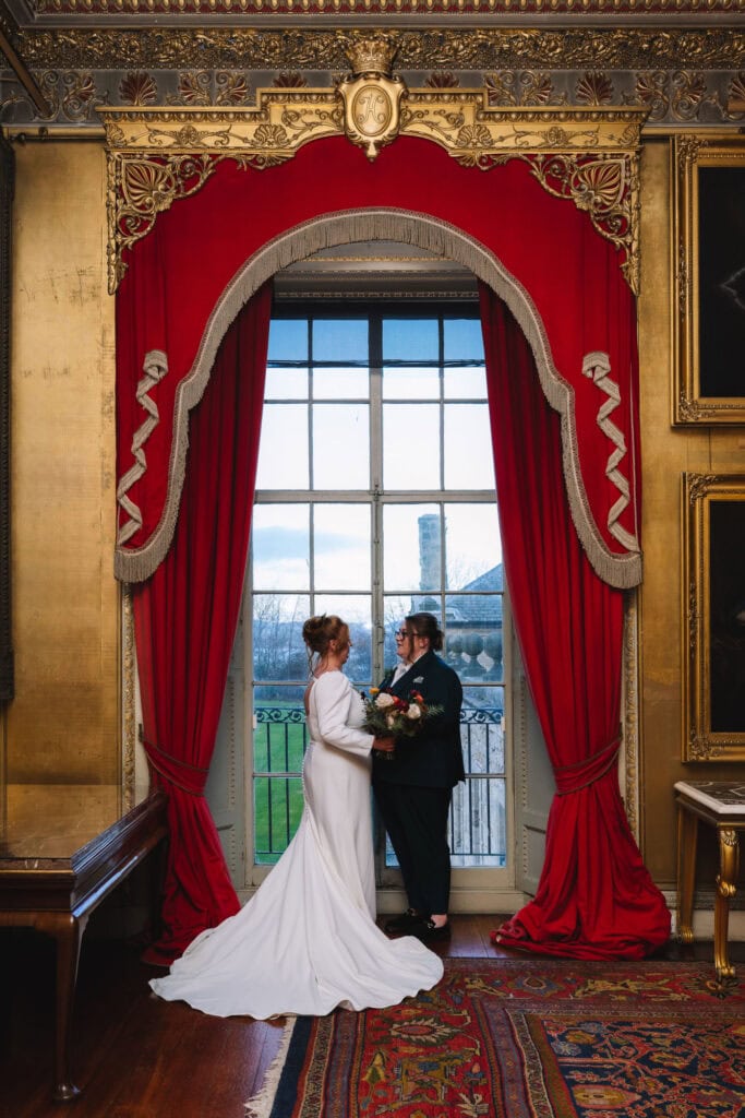 Couple framed by red curtains standing near window with outdoor view.