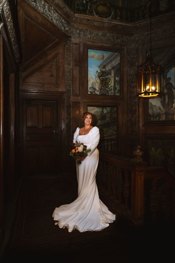Bride posing alone in wood-paneled room holding bouquet.