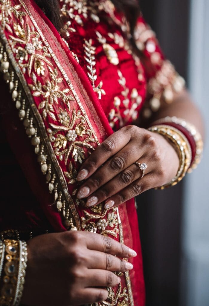 Close-up of bride’s hands with detailed jewelry and fabric.