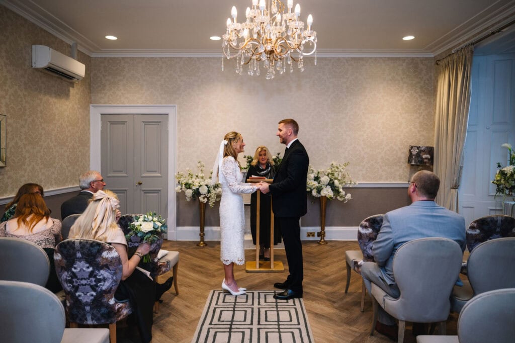 Couple exchanging vows during indoor ceremony with chandelier.
