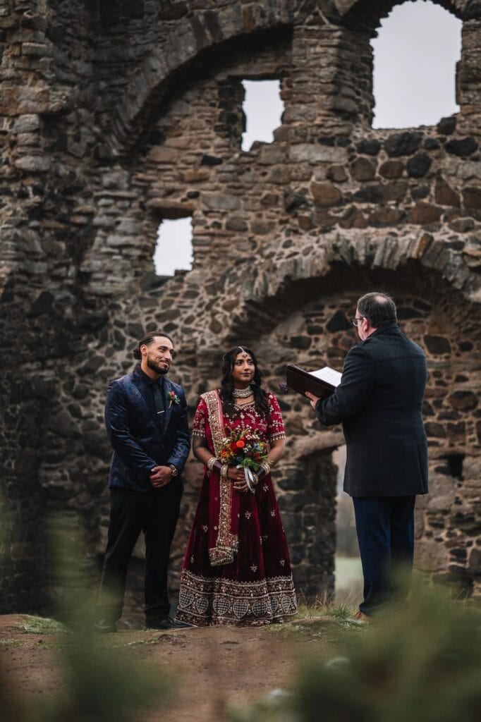 Ceremony scene with couple and officiant inside ruins.