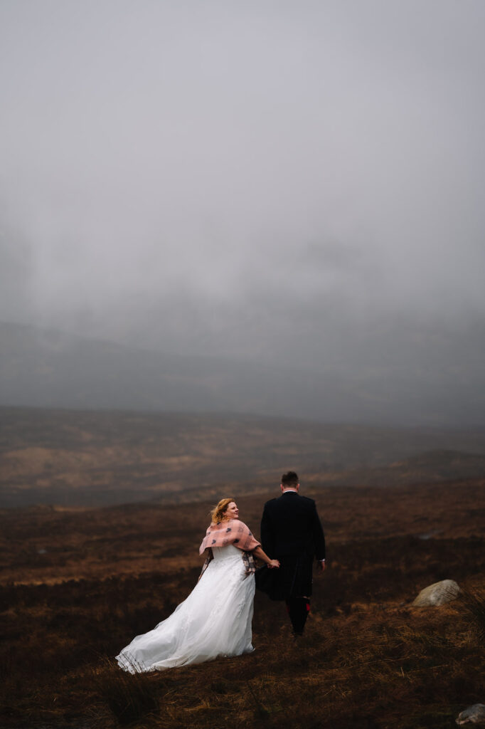 Couple walking away into misty landscape with mountains.