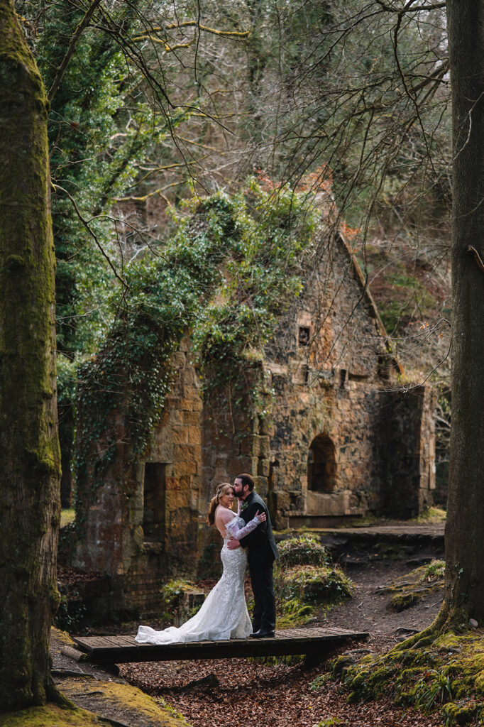 Couple embracing in overgrown ruin with moss and greenery.
