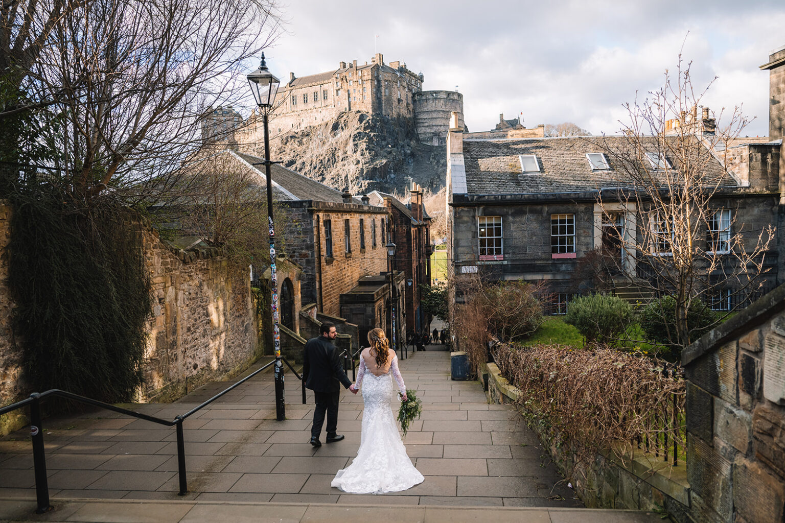 Couple walking through historic street with castle in distance.