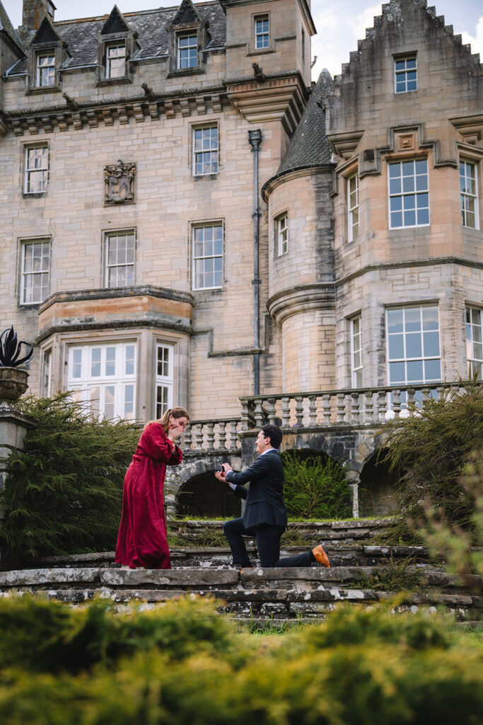 man proposing to woman on steps outside castle.