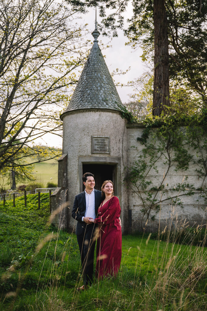 Couple standing in front of small turreted stone building.