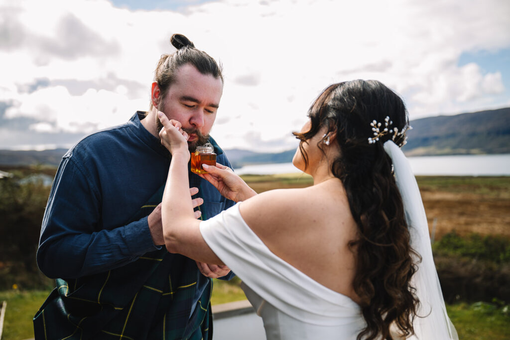 Bride feeding groom cake playfully during outdoor moment.