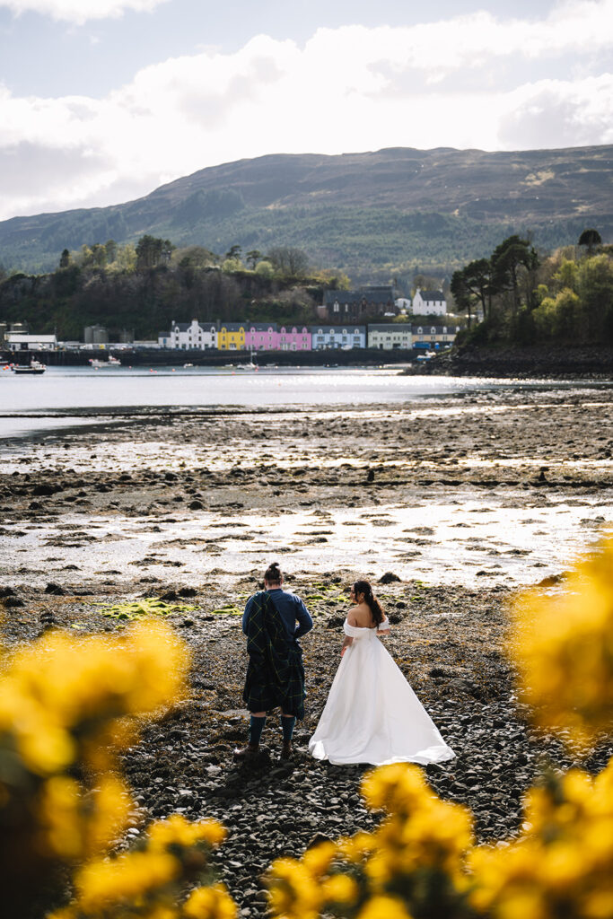 Couple walking across shoreline with water and hills behind.