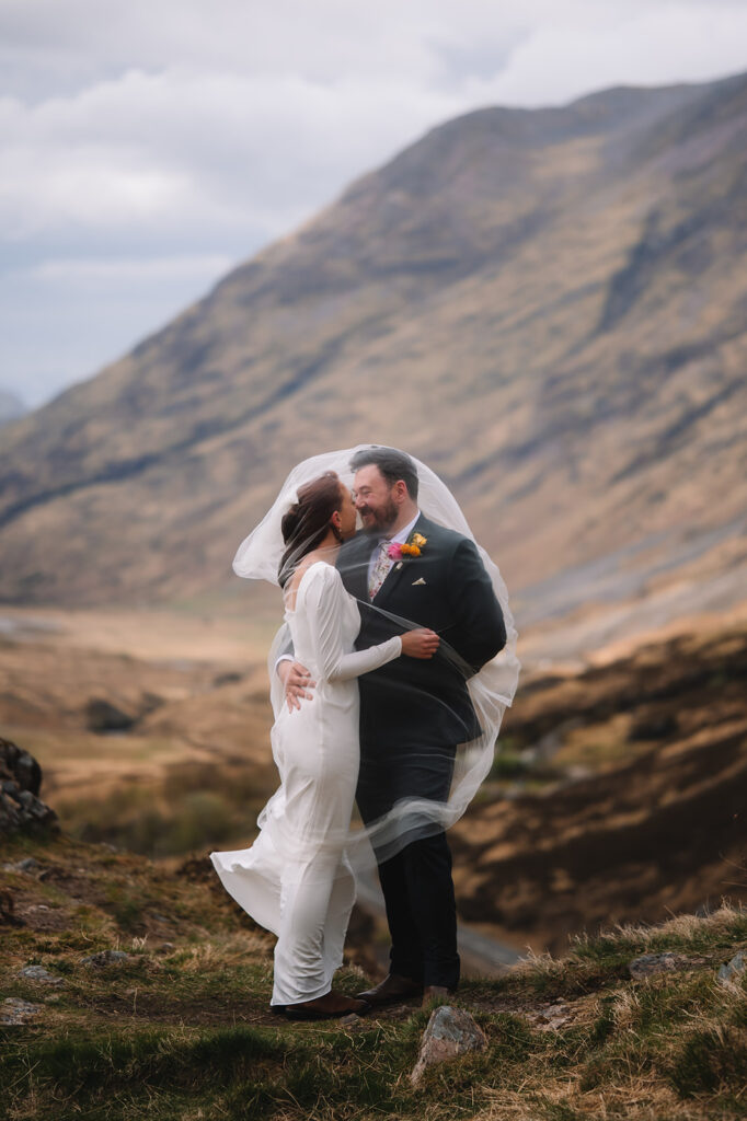 Couple embracing in warm-toned Highland landscape.
