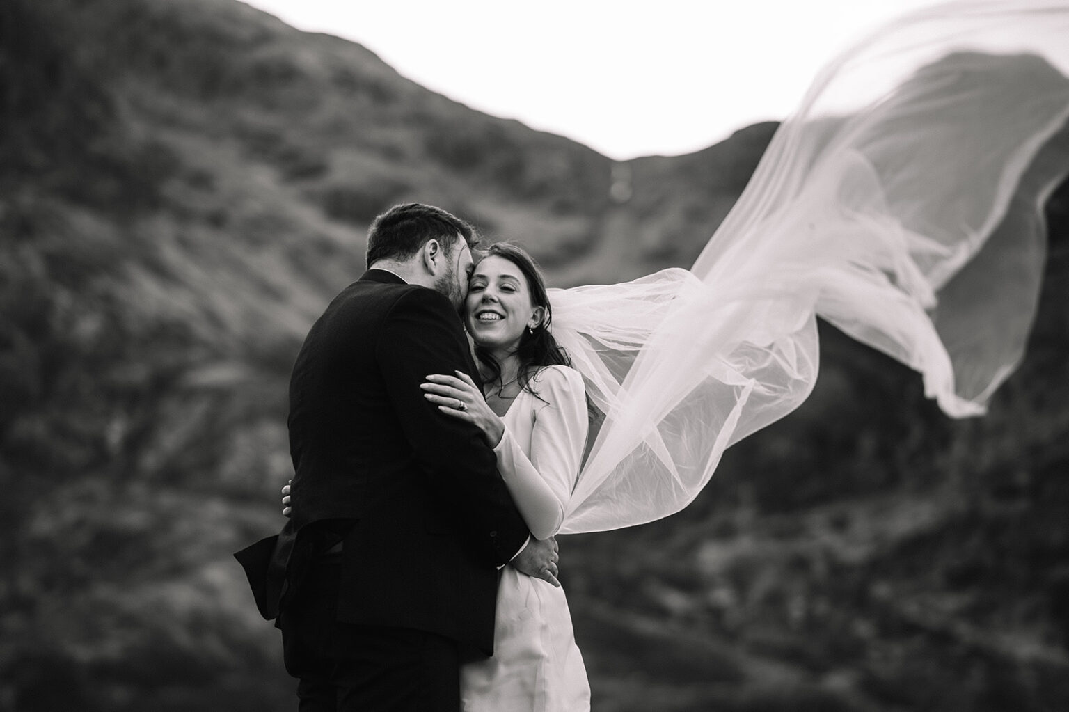 Black and white portrait of couple with veil flowing in wind.