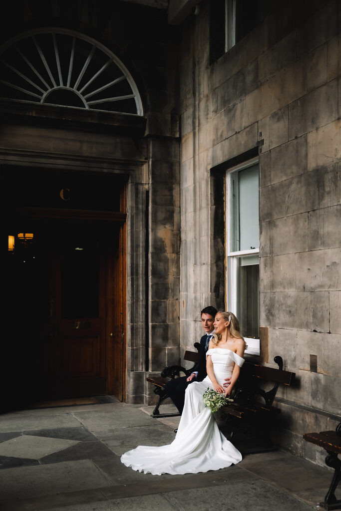 Bride sitting outside building in soft light.